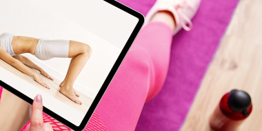 Persoon op yogamat bekijkt op tablet een bekkenbodemoefening