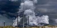 Windmolens op het strand met rokende fabrieksschoorstenen op de achtergrond