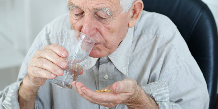 Oudere man met grijs haar neemt een handje pillen in met een glas water